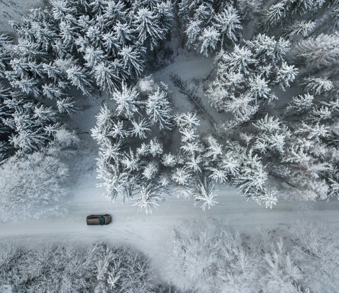 Drönarbild på vintrigt skogslandskap med en väg där en bil kör.